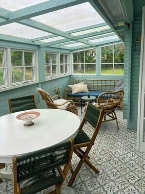 A conservatory with a round table and wicker chairs, a sofa, and a patterned floor. - Summer cottage with conservatory and enclosed plot (Nykøbing Sjælland)