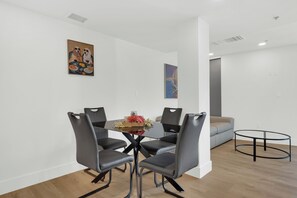 Een moderne eetruimte met een glazen tafel, omringd door vier stoelen, een klein middelpunt en twee schilderijen aan de muur.