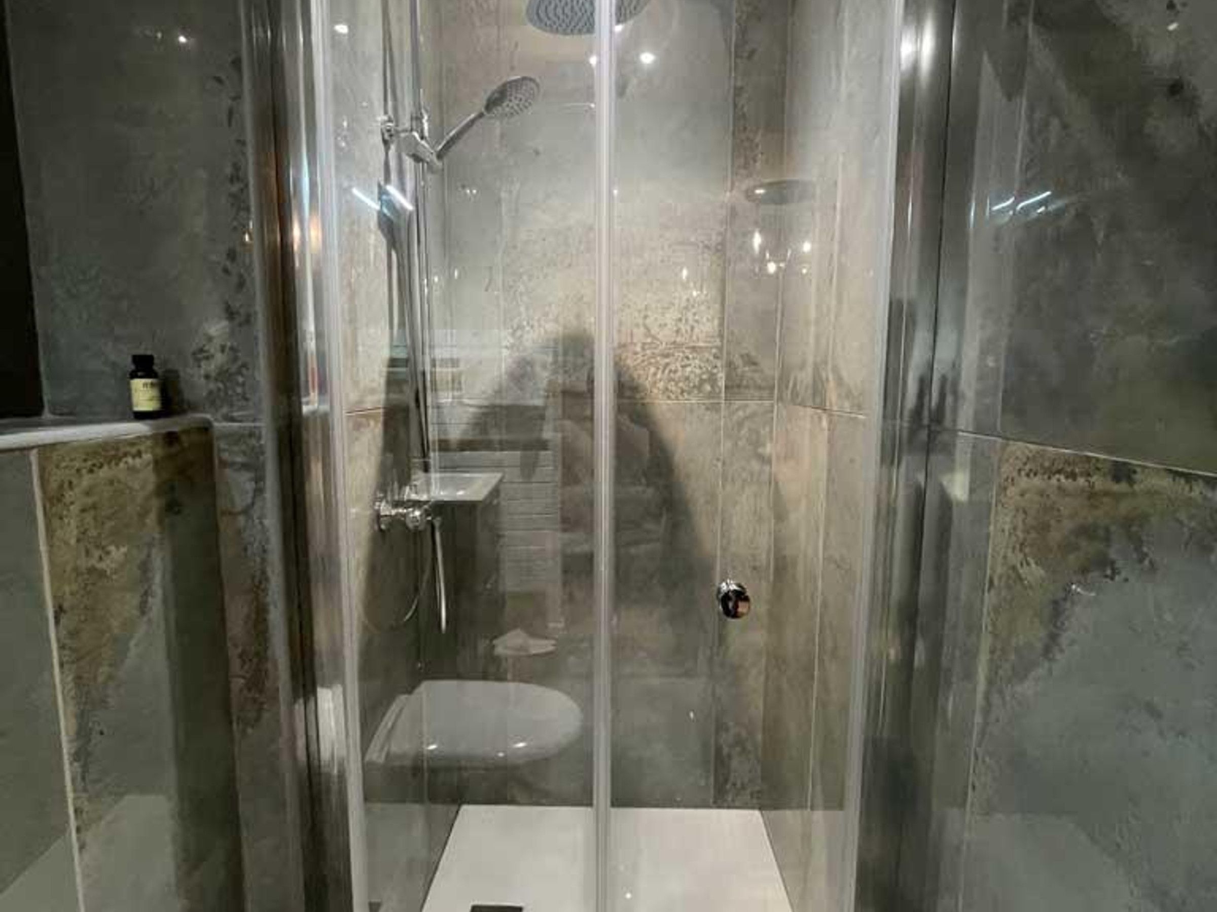 A glass-enclosed shower stall with a handheld showerhead and a wall-mounted faucet.