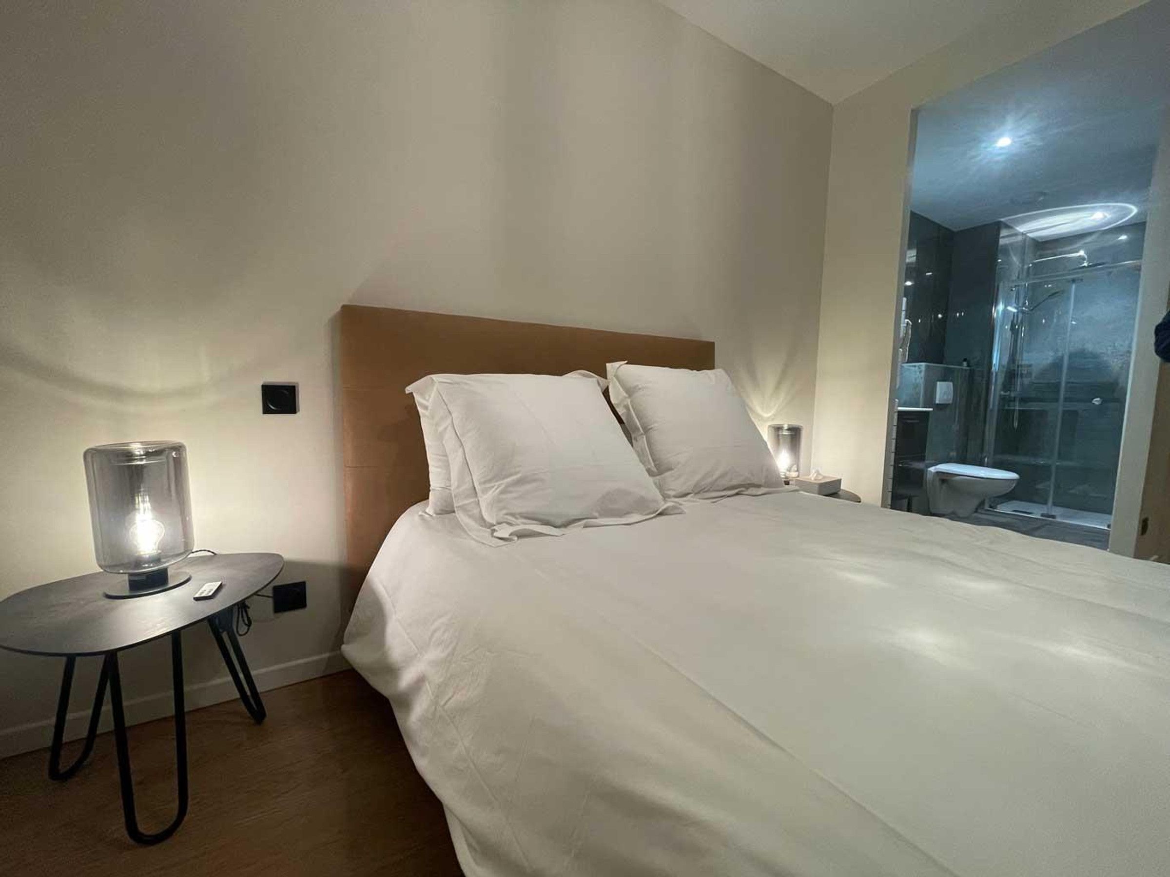 A hotel room with a bed, bedside tables, a mirror, and a shower area.