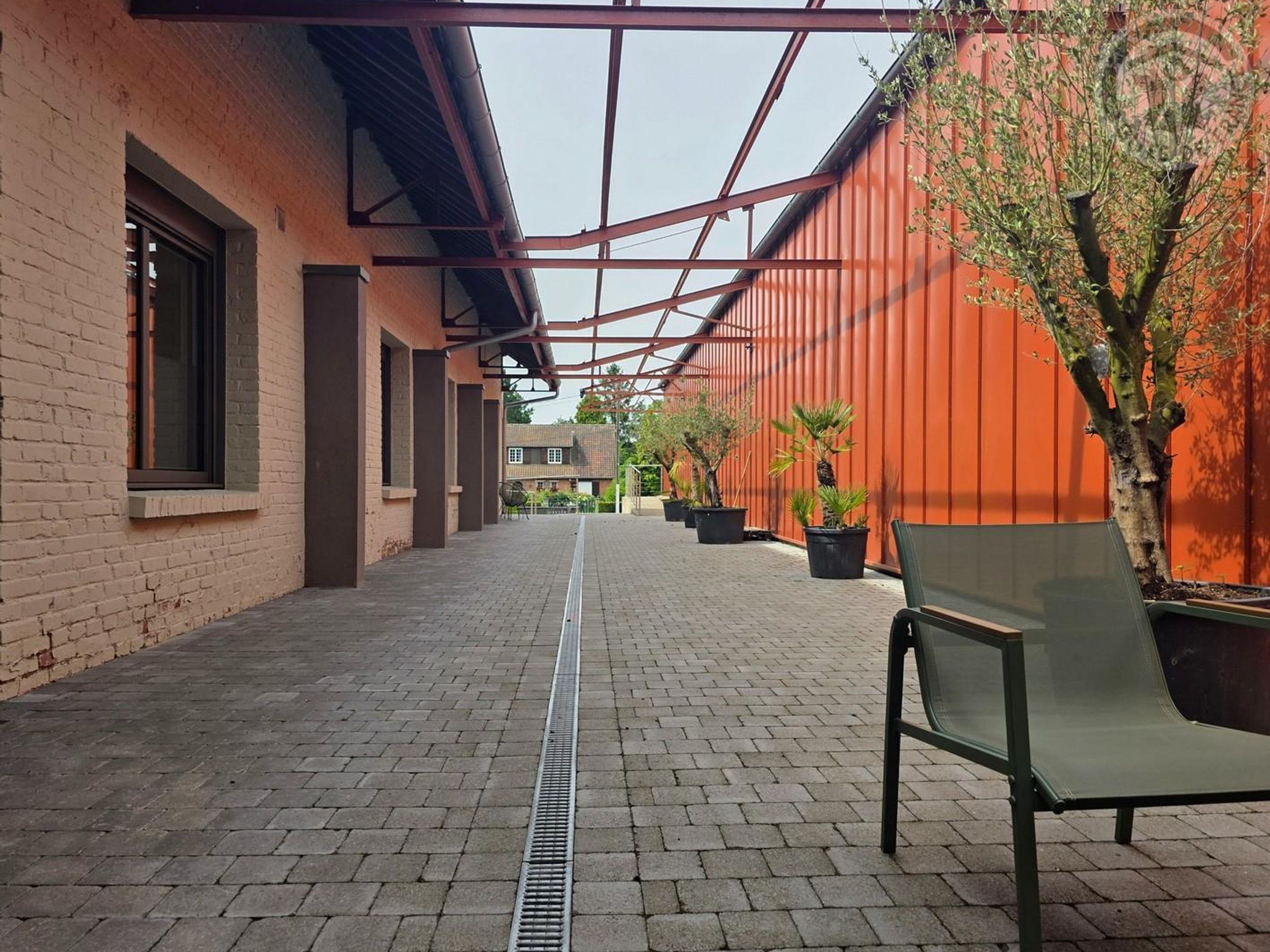 A covered walkway with brick flooring, potted plants, and a bench.