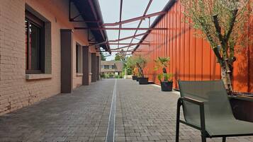A covered walkway with brick flooring, potted plants, and a bench.