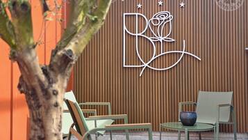 A wooden wall with a logo, a potted plant, and outdoor seating with chairs and a table.
