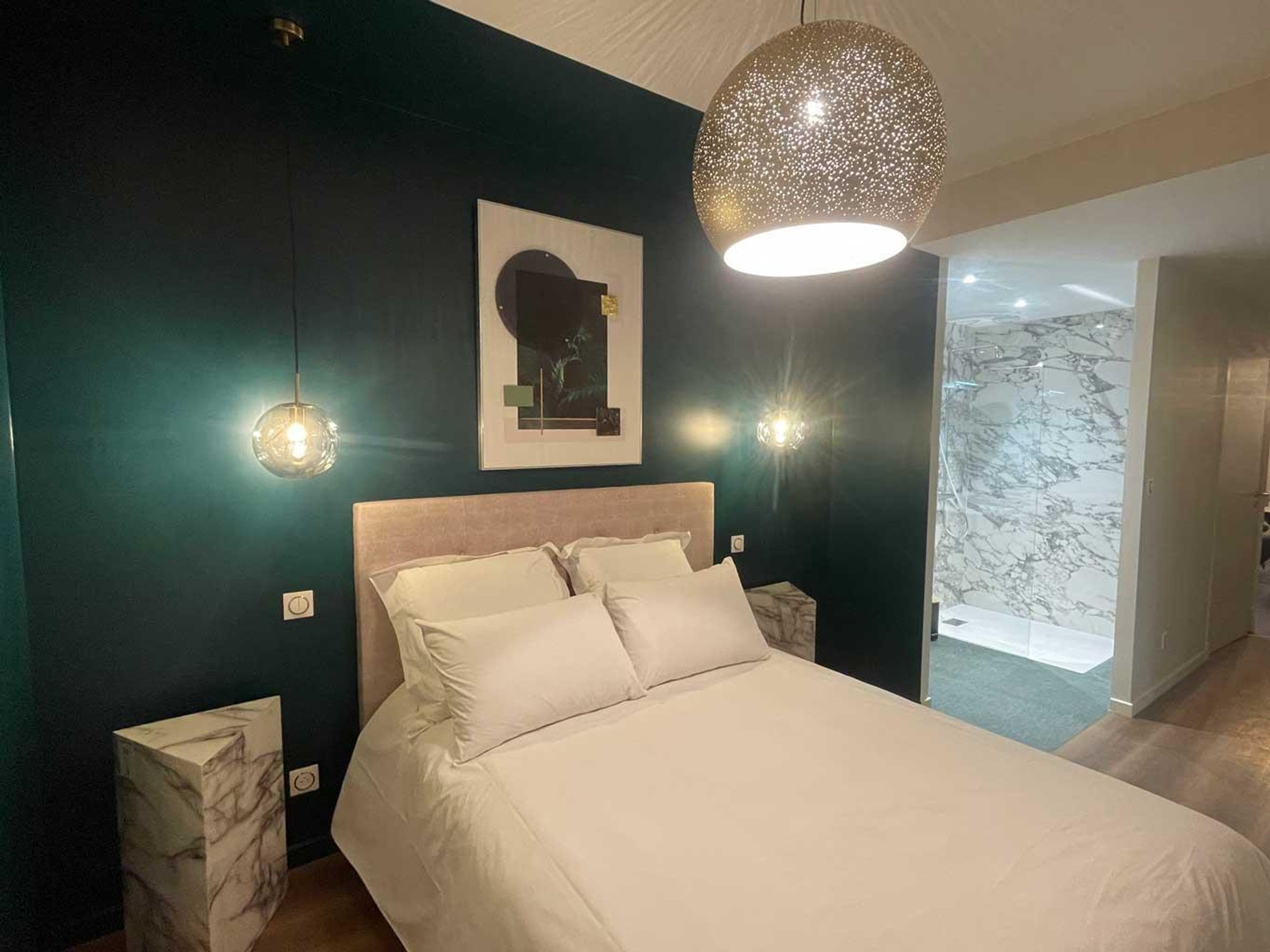 Une chambre à coucher avec un lit, deux lampes de chevet, un luminaire fixé au mur et un tableau encadré.