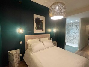 Een slaapkamer met een bed, twee bedlampen, een wandlamp en een lijst met een afbeelding.