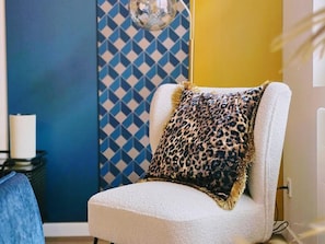 Una silla con un cojín estampado de leopardo, una pared con diseño y una lámpara blanca.