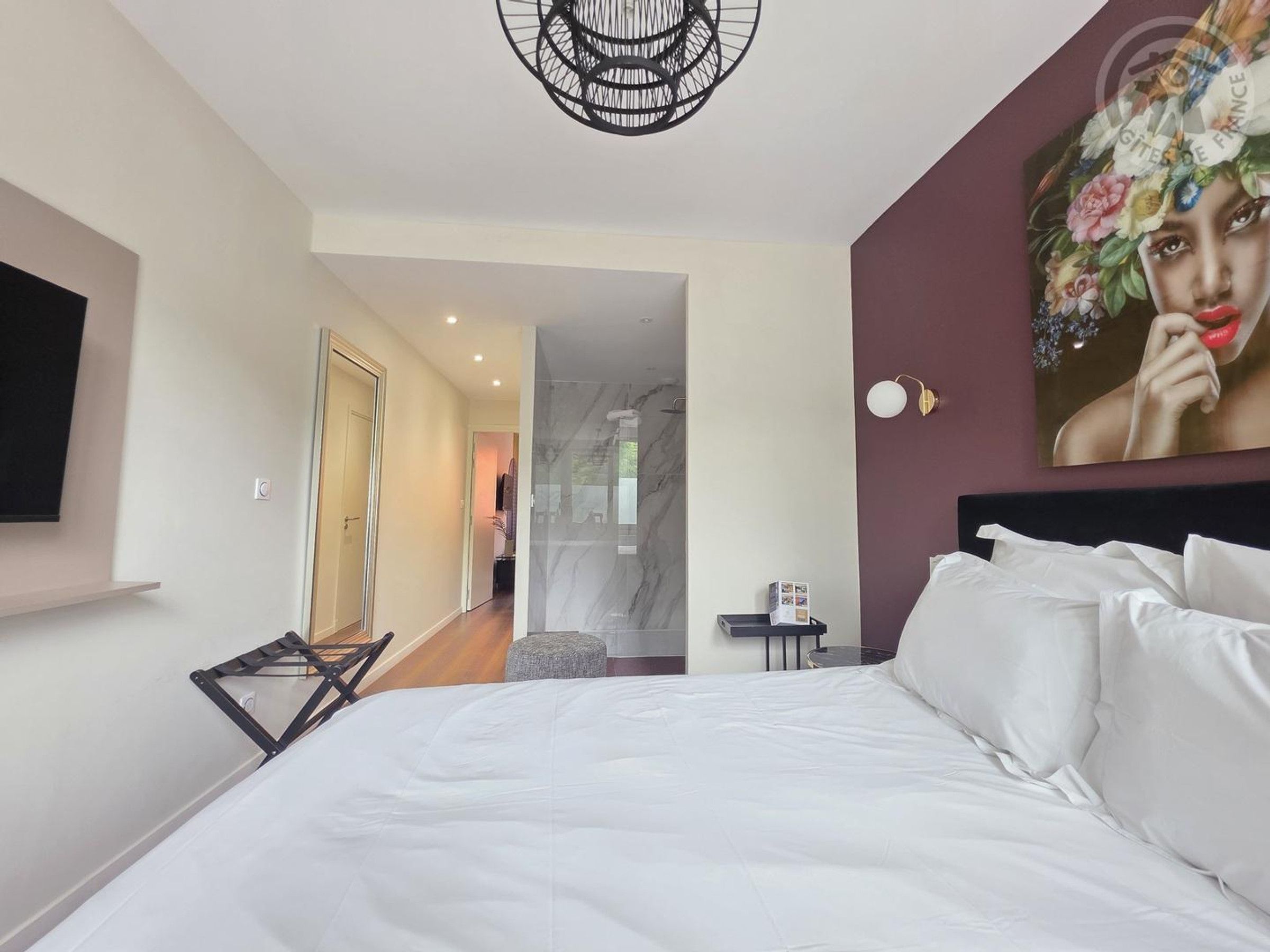 Een hotelkamer met een groot bed, een flatscreen televisie aan de muur, een schilderij boven het bed en uitzicht op de badkamer.