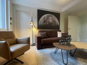 A modern living room with a sofa, armchair, and coffee table, featuring a large moon painting on the wall. - Ground-floor apartment in Niergnies - 2 guests (NIERGNIES)