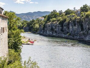 A river with boats, a stone building, and a cliff with vegetation. - Mobile home with AC - 4 guests (Joyeuse)