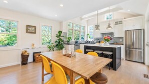 A modern kitchen with a wooden dining table, yellow chairs, and a stainless steel refrigerator. - Serene Water Mill Retreat with Hot Tub, Farm Views, & Lush Gardens, Perfect... (Water Mill)