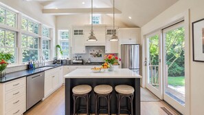 A modern kitchen with a central island, bar stools, and a view of the outdoors. - Serene Water Mill Retreat with Hot Tub, Farm Views, & Lush Gardens, Perfect... (Water Mill)