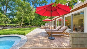 Une terrasse en bois avec une piscine, des chaises longues et des parasols rouges.