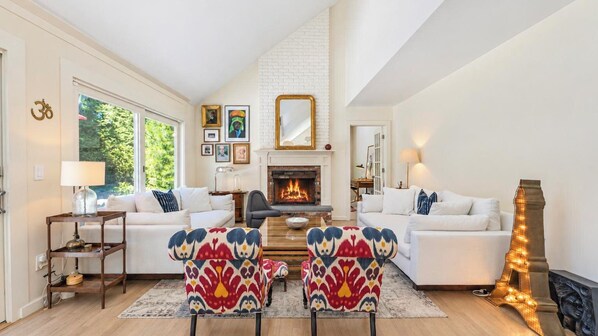 A living room with two white sofas, a fireplace, and colorful patterned chairs. - Serene Water Mill Retreat with Hot Tub, Farm Views, & Lush Gardens, Perfect... (Water Mill)