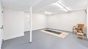 A room with a grey floor, a black mat, a white door, and a wicker chair with a cushion. - Serene Water Mill Retreat with Hot Tub, Farm Views, & Lush Gardens, Perfect... (Water Mill)