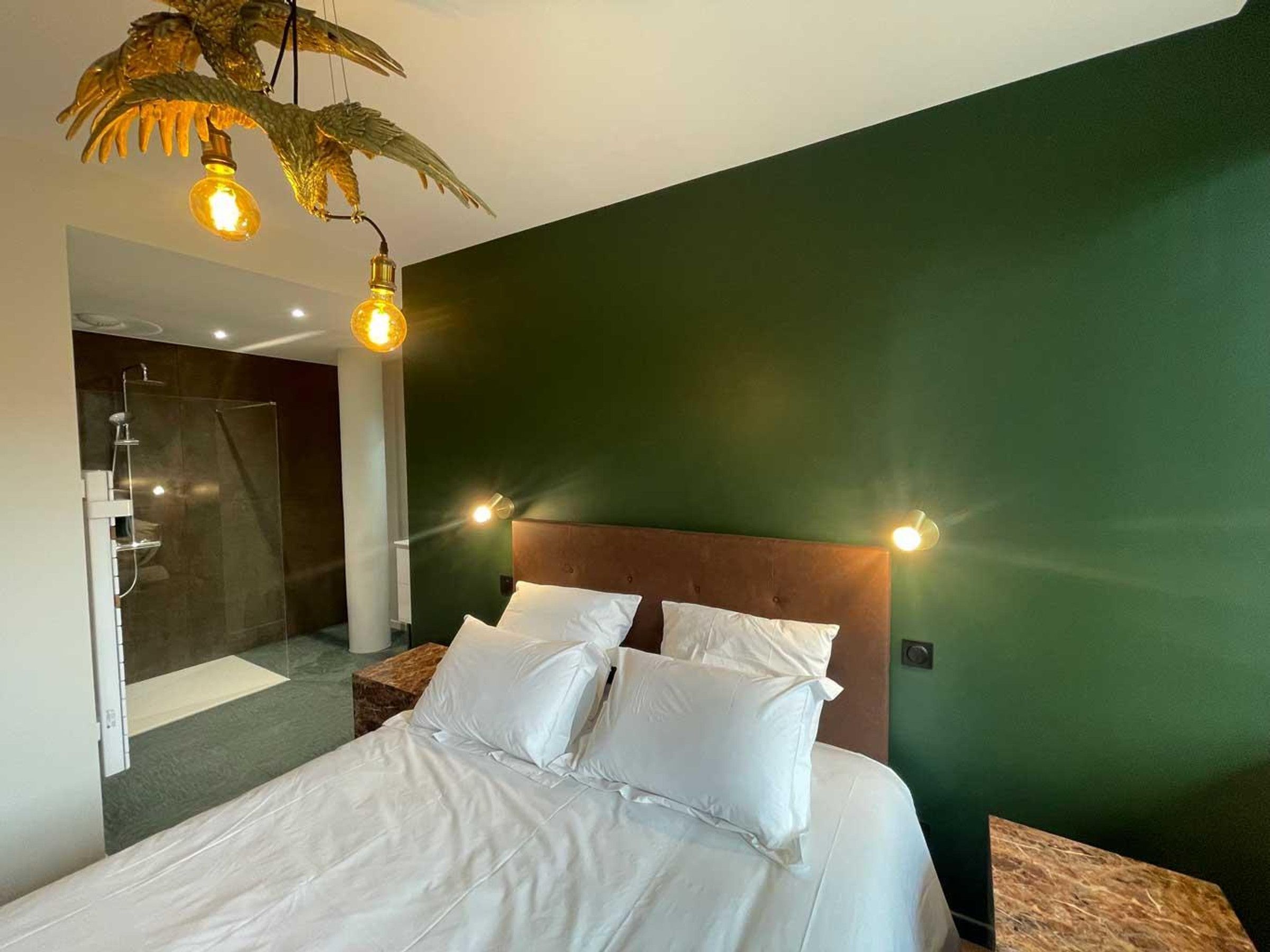 A hotel room with a bed, a shower, and a green wall.