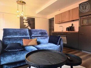 A modern living room with a blue sofa, a coffee table, and a kitchen area with wooden cabinets and a stainless steel refrigerator. - Modern and spacious apartment - 15 guests (NIERGNIES)