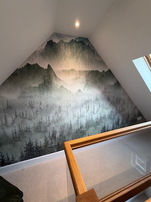 A room with a sloped ceiling, a wooden railing, and a mural of a forested mountain range. - The Scholars Nest Luxury Loft Gym Parking WiFi (Cambridge)