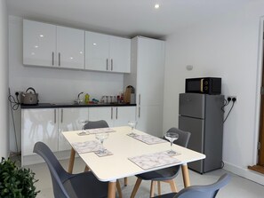A modern kitchen with white cabinets, a grey refrigerator, a dining table with chairs, and a small potted plant. - The Scholars Nest Luxury Loft Gym Parking WiFi (Cambridge)