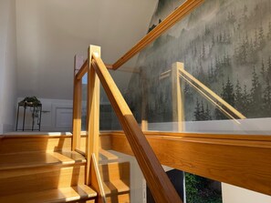 A staircase with wooden railings and a glass balustrade, leading to a room with a mountain landscape mural. - The Scholars Nest Luxury Loft Gym Parking WiFi (Cambridge)