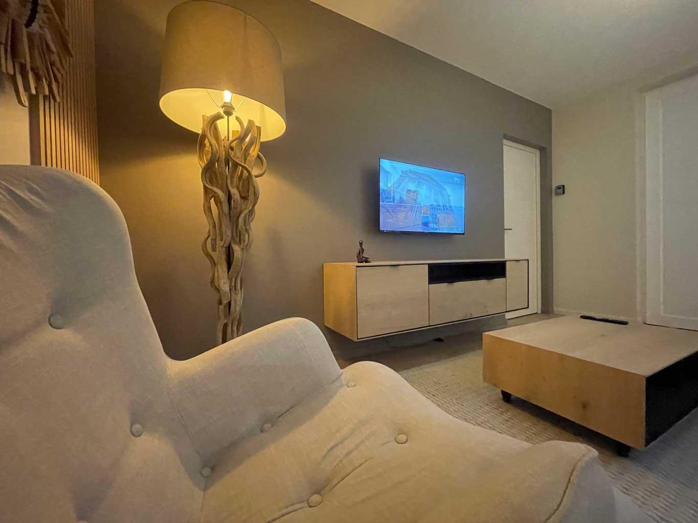 A modern living room with a large armchair, a television on a wall, and a wooden cabinet.