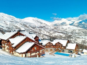 A snow-covered mountain village with wooden buildings and a pool. - 3-room apartment mountain view - 6 guests (Le Corbier)