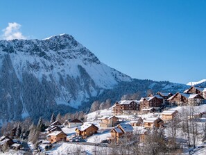 Ett snötäckt berg med klar himmel, omgivet av trähus med sluttande tak, troligen en skidort.
