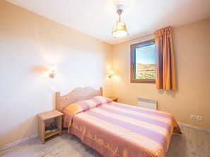 A bedroom with a bed, bedside lamps, a nightstand, a window with a view, and a ceiling light fixture. - 3-room apartment mountain view - 6 guests (Le Corbier)
