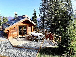 A wooden cabin with a sloped roof, a deck with picnic tables, and a gravel ground. - Mountain chalet ski-in/ski-out - 8 guests (Courchevel)