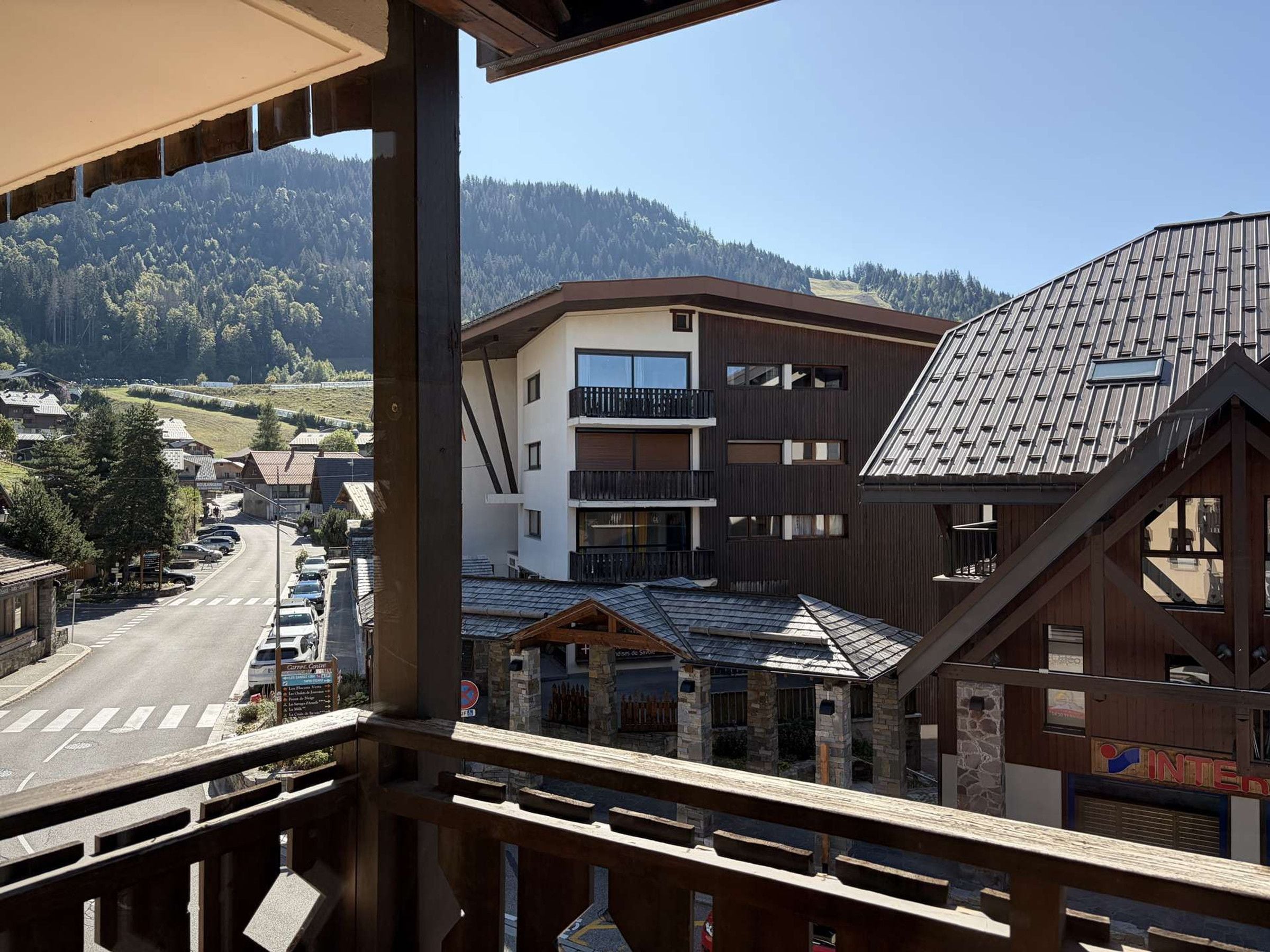 A multi-story building with balconies, a parking lot, and a view of a mountainous area.