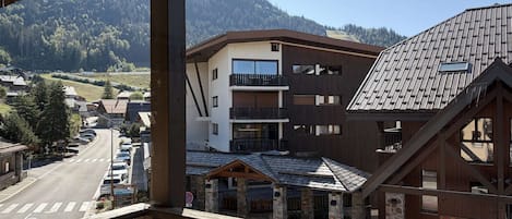 A multi-story building with balconies, a parking lot, and a view of a mountainous area.