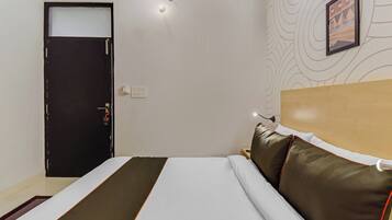 A hotel room with a bed, a door, a wall-mounted light, and a framed picture.