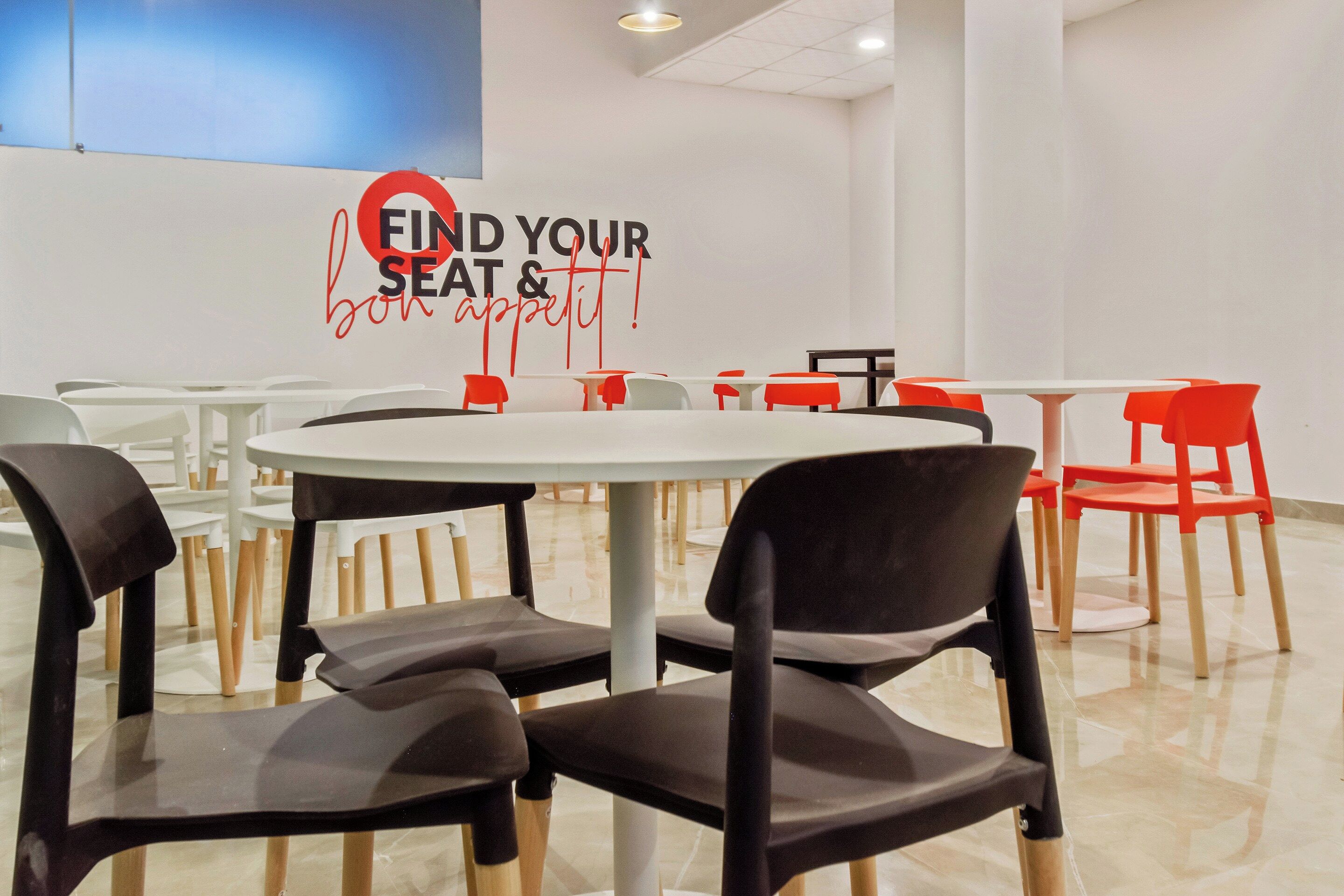 A dining area with round tables and chairs, a wall with a sign that reads 'FIND YOUR seat & bon appétit!', and a blue accent wall.