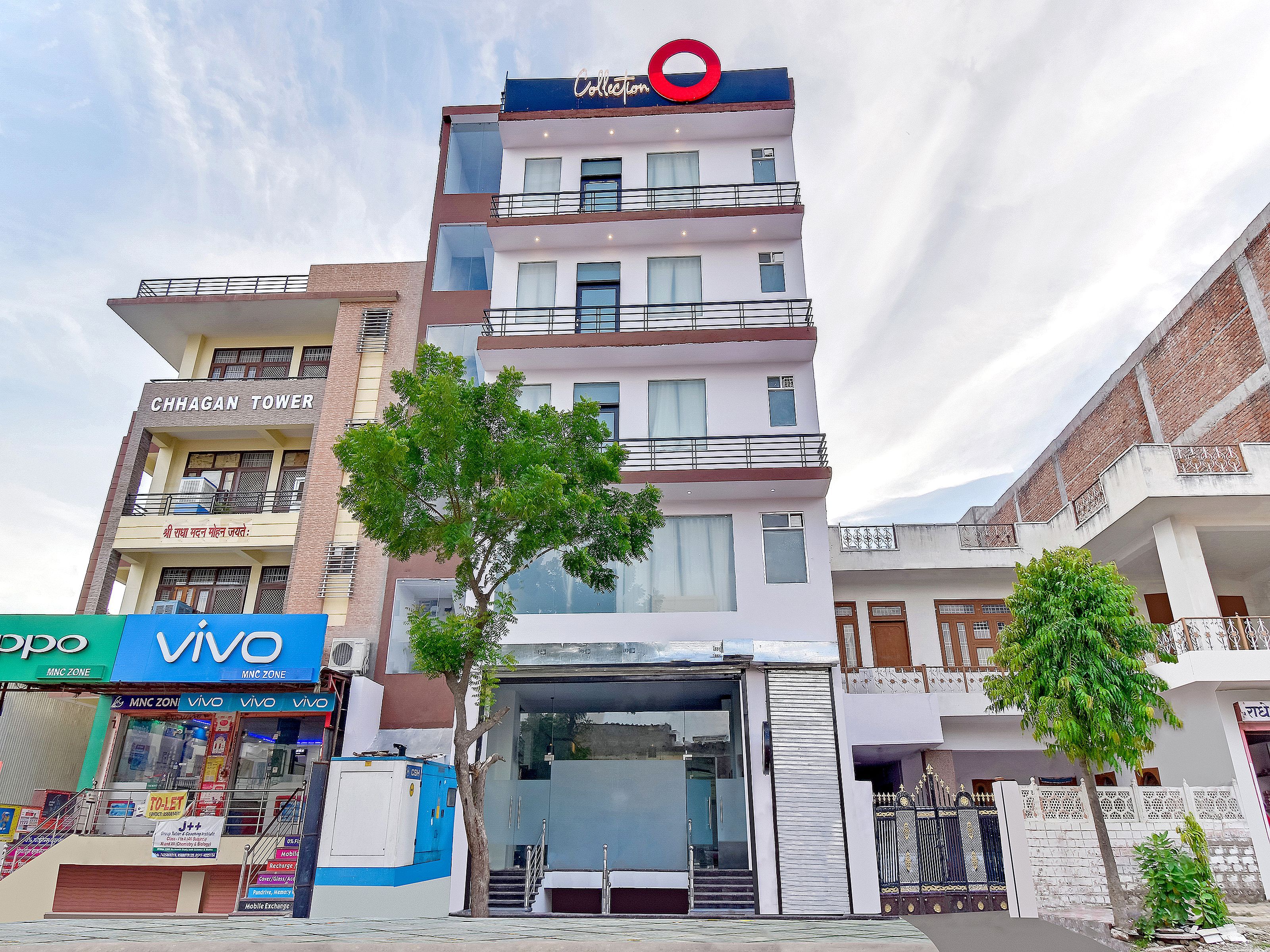 A multi-story building with balconies, a prominent red circular sign, and a tree in front.