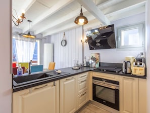 A modern kitchen with white cabinetry, a black countertop, a built-in oven, and a microwave. There are hanging pendant lights and a clock on the wall. - Charming apartment with terrace - 4 guests (Cauterets)