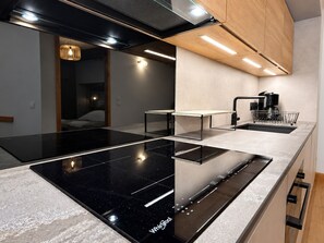 A modern kitchen with a black induction cooktop, a coffee machine, and a built-in oven. - Apartment with parking - 4 guests, village view (Champagny-en-Vanoise)