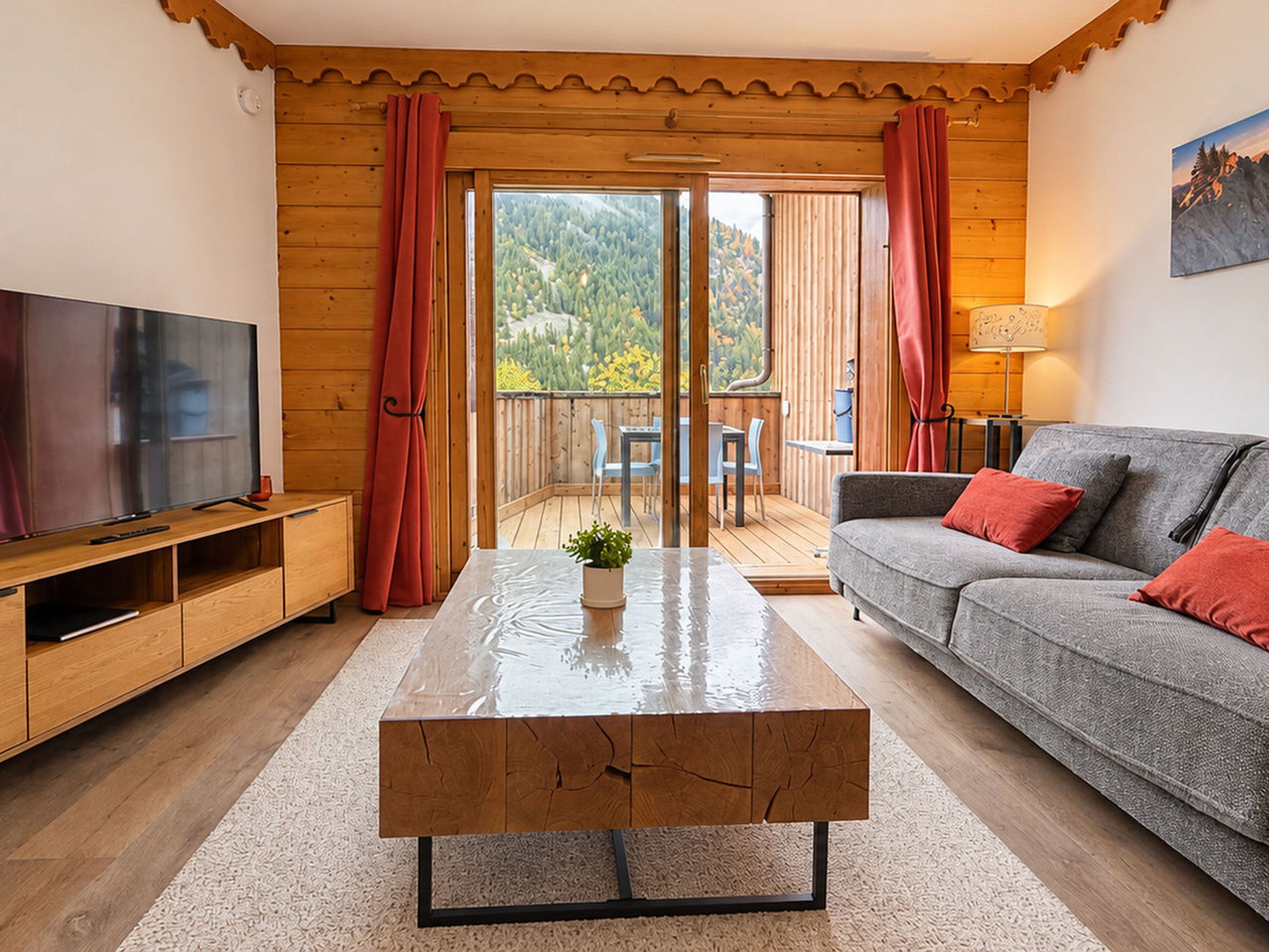 A living room with a television, sofa, coffee table, and a view of a balcony with outdoor seating.
