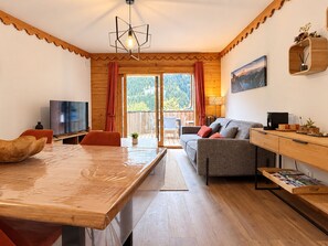 A modern living room with a wooden dining table, sofa, and a television. - Apartment with parking - 4 guests, village view (Champagny-en-Vanoise)