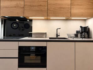 A modern kitchen with wooden cabinets, a black oven, a sink, and a coffee maker. - Apartment with parking - 4 guests, village view (Champagny-en-Vanoise)