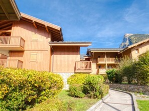 A wooden chalet with balconies, a stone pathway, and a mountain backdrop. - Cozy duplex with parking - 8 guests (Samoëns)