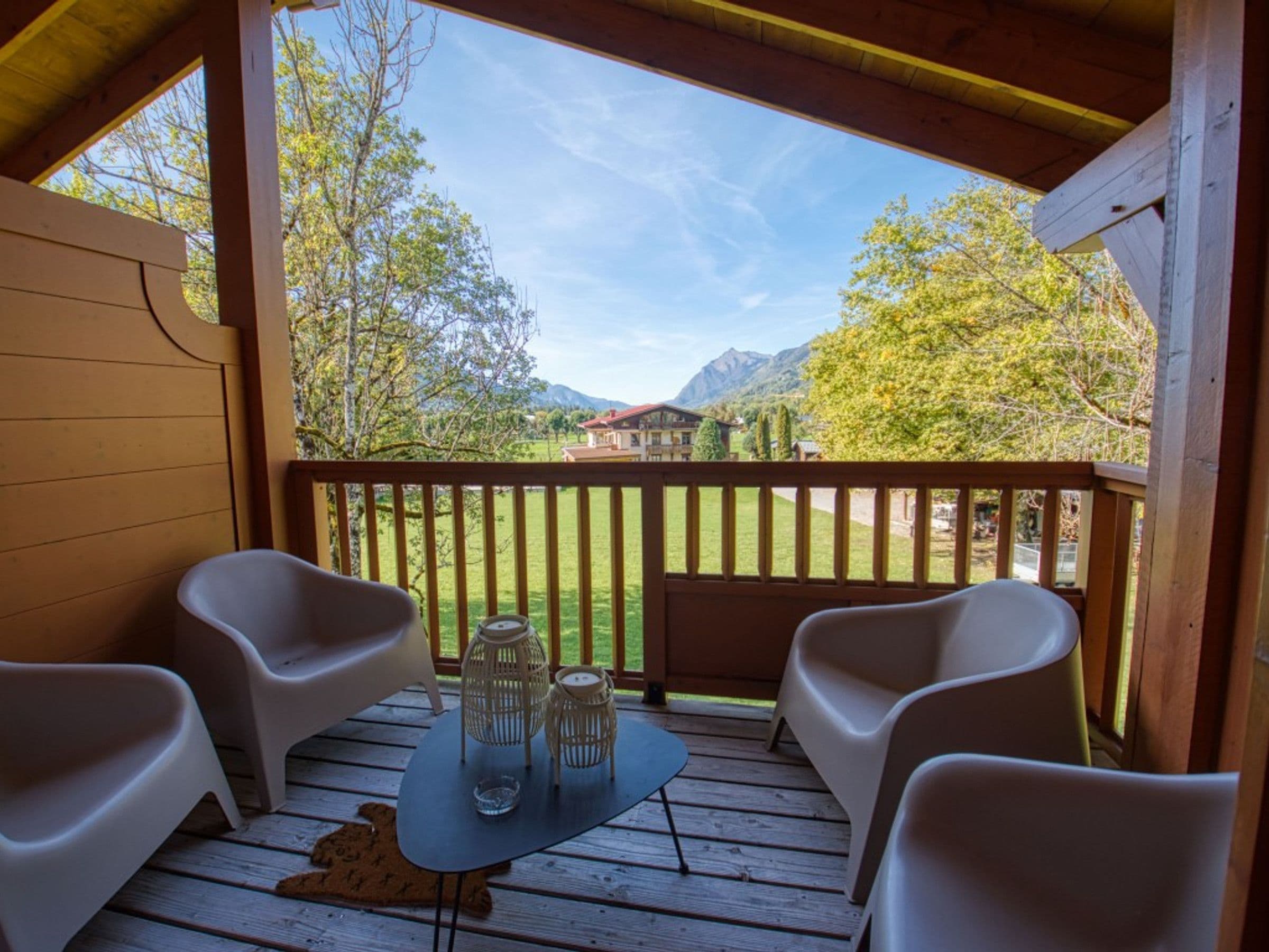 A wooden deck with two white chairs and a table, overlooking a grassy area with trees and buildings in the distance.