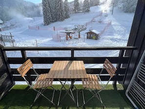 A balcony with a wooden table and chairs overlooking a snow-covered ski slope with a ski lift. - Apartment with parking - 5 guests, Morillon (Morillon)