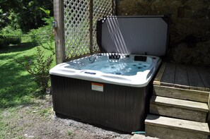 A hot tub with a control panel, surrounded by a wooden deck and a stone wall. - Whispering Cascade Creek-peaceful and romantic (Hot Springs)