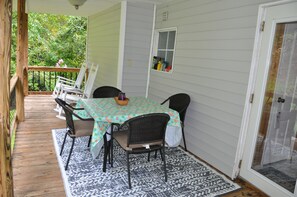 A covered patio with a table and chairs, a wooden deck, and a view of greenery. - Whispering Cascade Creek-peaceful and romantic (Hot Springs)