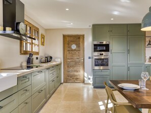 A modern kitchen with a wooden door, stainless steel appliances, and a dining area with a table set for two. - Chalet at the foot of the slopes with sauna - 15 guests (Les Saisies)