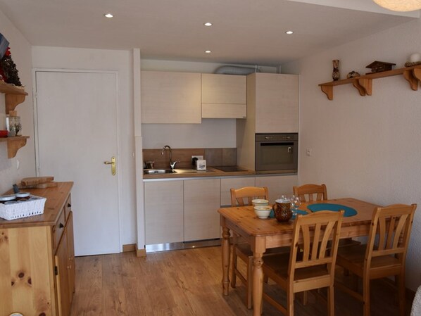 A compact kitchen with white cabinets, a wooden dining table with four chairs, and a built-in oven. - Central apartment - 6 guests (Montgenèvre)