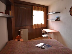 A bedroom with a bed, a desk, a chair, a radiator, and a window with curtains. - Central apartment - 6 guests (Montgenèvre)