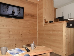 A wooden interior with a television mounted on the wall, a small shelf with a figurine, and a table with a remote control and a mug. - Apartment balcony mountain view - 4 guests (Montgenèvre)
