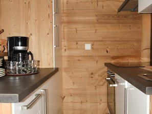 A kitchen with wooden paneling, a coffee maker, and glasses on the counter. - Apartment balcony mountain view - 4 guests (Montgenèvre)