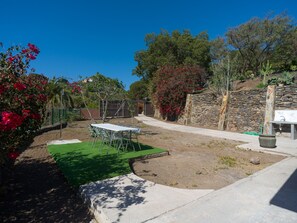 Ein Terrassenbereich im Freien mit Tisch und Stühlen, umgeben von einer Steinmauer und verschiedenen Pflanzen.