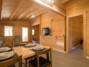 Un intérieur en bois comprenant un coin repas, un téléviseur fixé au mur et une porte donnant sur une autre pièce.